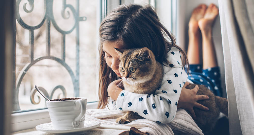 girl-holding-cat-on-window-sill