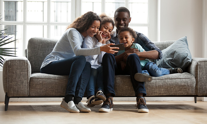 happy-american-family-sitting-on-couch-looking-at-phone-at-home