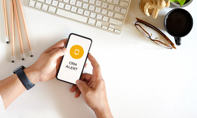 holding-cell-phone-crm-alert-desk-flat-lay-computer-key-board-glasses-mug