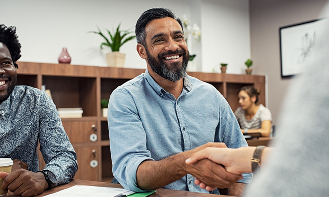 man-shaking-hand-in-meeting-light-blue-shirt-dark-beard