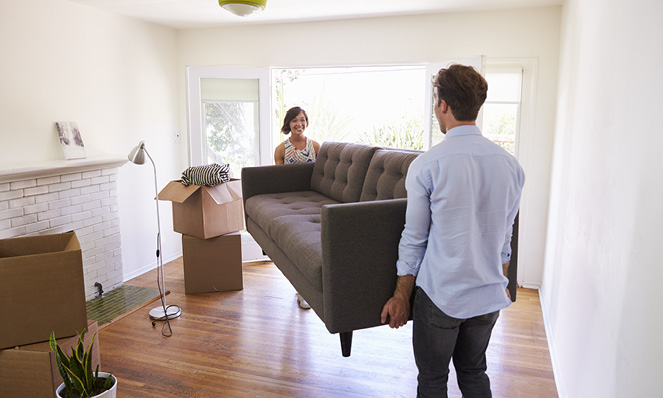 couple-moving-grey-sofa-into-living-room-wood-floors