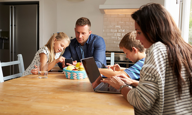 family-of-four-looking-at-technology-in-kitchen