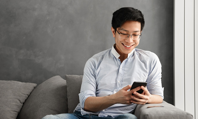 man-smiling-looking-at-phone-grey-sofa-wall