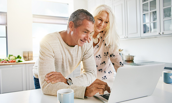 older-couple-looking-at-laptop-kitchen-beige-sweater-pink-foral-blouse
