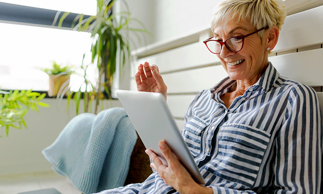 older-woman-smiling-at-tablet-at-home-striped-shirt-light-blue-blanket