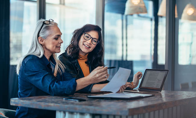 older-woman-talking-to-younger-woman-in-cafe-with-papers-and-laptop