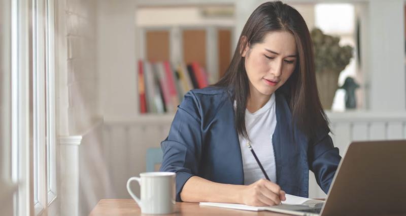 woman-writing-on-paper-laptop-coffee-mug