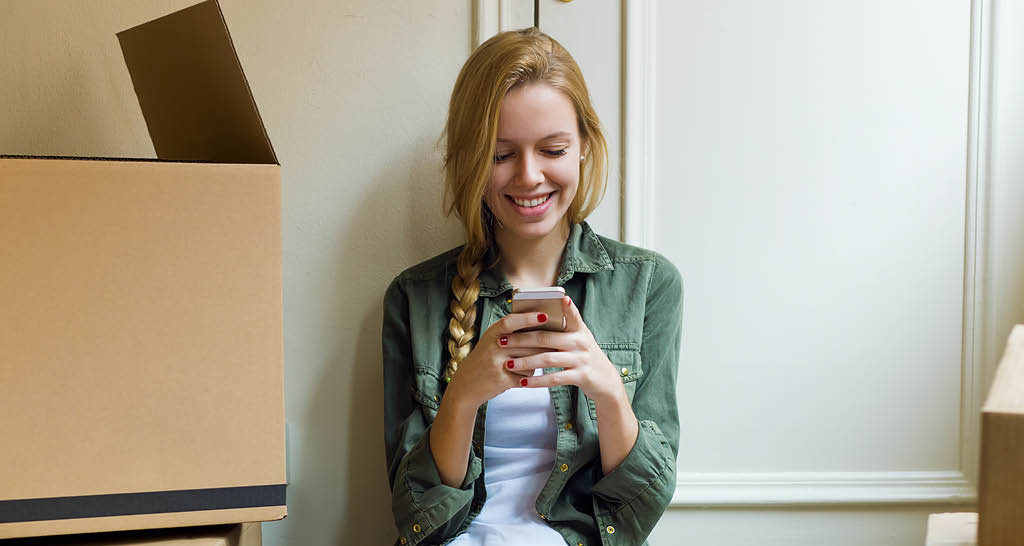 young-woman-looking-at-phone-green-shirt-moving-boxes