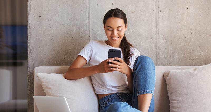 young-woman-sitting-at-home-looking-at-phone-white-t-shirt-blue-jeans